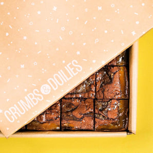 Salted Caramel Brownie by Crumbs & Doilies in a branded box with caramel swirls and sea salt on top.